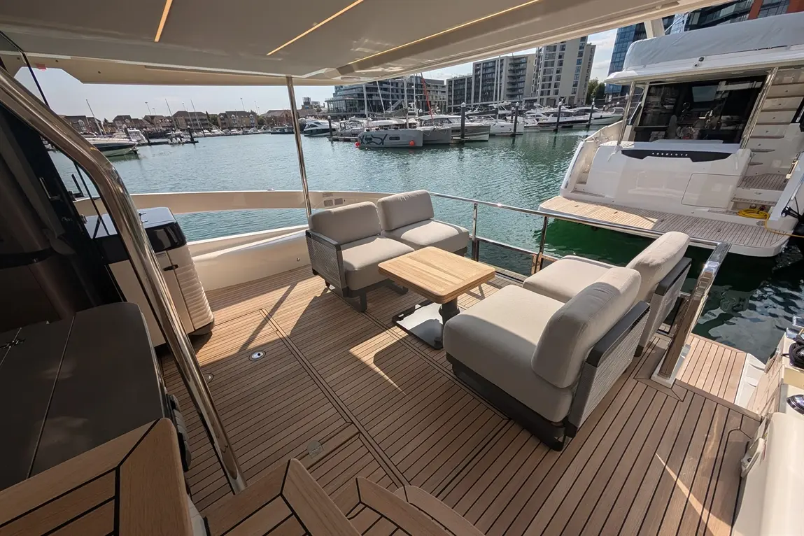 Luxury yacht deck featuring a seating area with cushions, a wooden table, and views of boats in the marina.